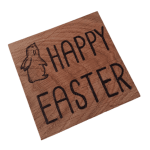 A square wooden coaster featuring intricate oak woodwork with the words 'Happy Easter' engraved on the surface in elegant script. The coaster is handcrafted with attention to detail, showcasing the warmth and natural beauty of wood grain. Hand burnt with a Hare design