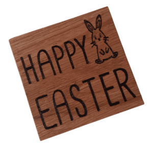 A square wooden coaster featuring intricate oak woodwork with the words 'Happy Easter' engraved on the surface in elegant script. The coaster is handcrafted with attention to detail, showcasing the warmth and natural beauty of wood grain. Hand burnt with a Hare design