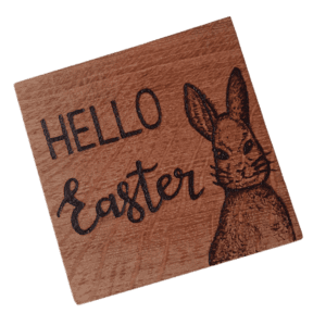 A square wooden coaster featuring intricate oak woodwork with the words 'Happy Easter' engraved on the surface in elegant script. The coaster is handcrafted with attention to detail, showcasing the warmth and natural beauty of wood grain. Hand burnt with a Hare design