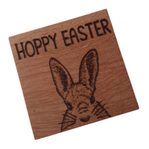 A square wooden coaster featuring intricate oak woodwork with the words 'Hoppy Easter' engraved on the surface in elegant script. The coaster is handcrafted with attention to detail, showcasing the warmth and natural beauty of wood grain. Hand burnt with a Hare design