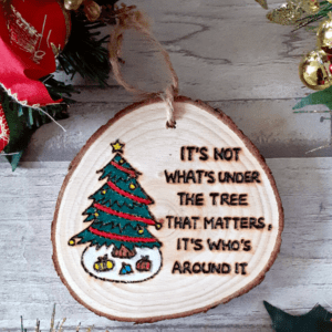 wood slice tree decoration with hand burnt text saying 'its not what's under the tree that matters, it's who's around it'