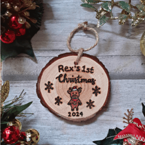 A personalized rustic Christmas tree ornament for a baby's 1st Christmas in 2024. The ornament features a hand-burnt reindeer design on a wooden surface. The reindeer is intricately crafted, showcasing antlers, a gentle face, and a joyful expression. The rustic charm is enhanced by the wood's natural grain and texture. The ornament is delicately engraved with the baby's name and '1st Christmas' to commemorate this special occasion. It hangs gracefully from jute rope, ready to add warmth and merriment to any Christmas tree