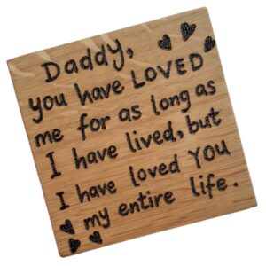 A square handmade wooden coaster made of oak. The coaster features a hand-burnt inscription that reads "Daddy, you have loved me" in a charming, rustic font. The wood's natural grain and texture are visible, adding to its artisanal and heartfelt appearance.