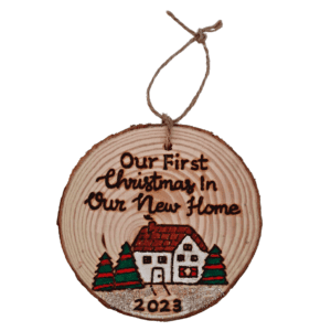 A charming rustic Christmas tree ornament featuring a festive house design. The ornament is shaped like a cozy home with a chimney, adorned with festive decorations. The text on the ornament reads, "Our First Christmas in Our New Home 2023," signifying a special celebration of a couple or family commemorating their first Christmas in their new house.