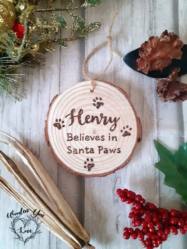 A rustic hanging slice with hand-burnt personalization featuring a pet's name and the phrase 'believes in Santa Paws'. Perfect for cats or dogs.