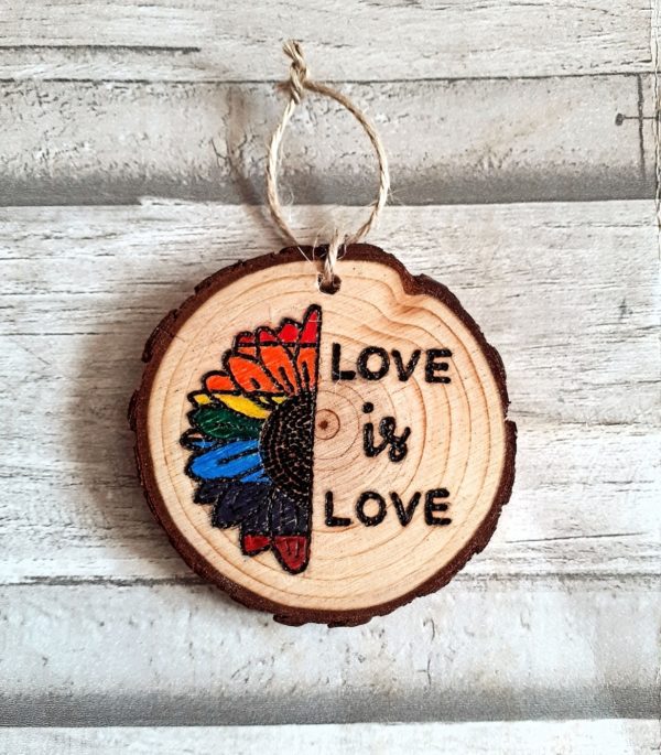 A hand-burnt wood slice featuring a half rainbow design and the phrase "Love is Love."