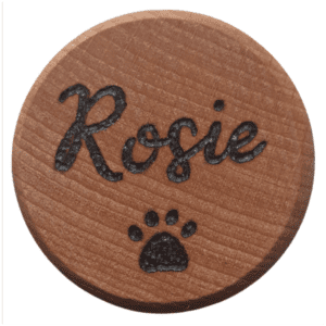 A close-up photograph of a handmade wooden pet fur memorial keepsake box. The box features intricate burnt designs on its surface, including paw prints and name of the pet. The wood appears rich and textured, with varying shades and grains. The craftsmanship is evident, showcasing a heartfelt tribute to a beloved furry companion