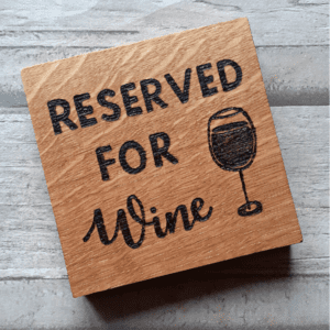 A square oak coaster featuring hand-burnt text that reads 'reserved for wine.' The coaster showcases a natural wood grain pattern, with a rich brown color and a smooth, polished surface. The text is carefully engraved with intricate detail, adding a touch of whimsy to the design. The coaster serves as a functional and decorative piece, perfect for holding a glass of wine while adding a playful and humorous element to any setting."