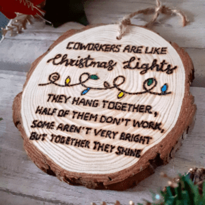 wood slice tree decoration with hand text which reads 'coworkers are like christmas lights they hang together half of them don't work some aren't very bright but together they shine'