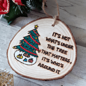 wood slice tree decoration with hand burnt text saying 'its not what's under the tree that matters, it's who's around it'
