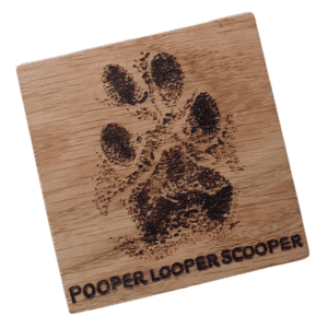 A square handmade wooden coaster made of oak. The coaster features a hand-burnt paw print and personalised with a name. The wood's natural grain and texture are visible, adding to its artisanal and heartfelt appearance.