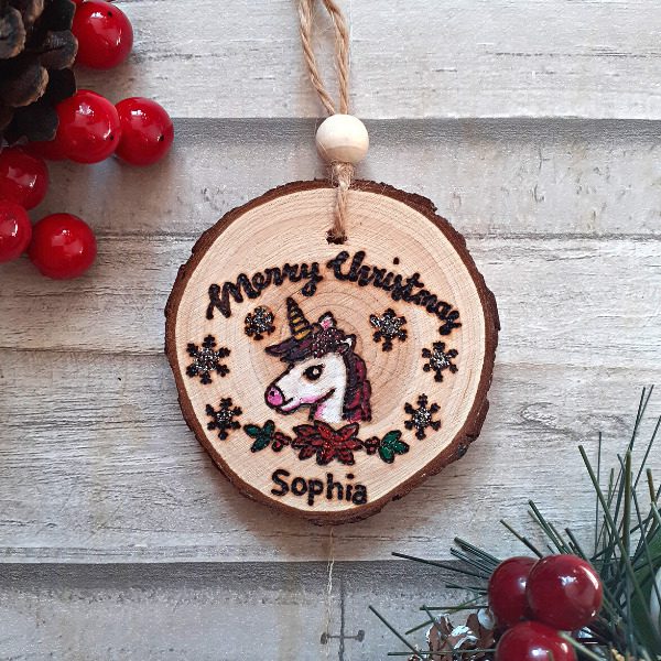 handmade wooden unicorn christmas ornament with a unicorn head and personalised with a name. A touch of glitter has been added to the snowflakes.