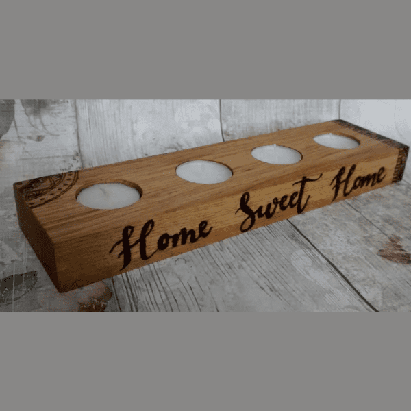 A wooden tea lighter holder made of oak, showcasing a handcrafted design with the words 'home sweet home' burned into the surface. The text is elegantly displayed and adds a warm, personal touch to the holder. The rich texture and natural wood grain of the oak complement the heartfelt message, making it a delightful addition to any home decor."