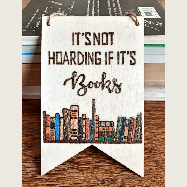 A sign with a hand-burnt bookshelf design that reads, "It's not hoarding if it's books."