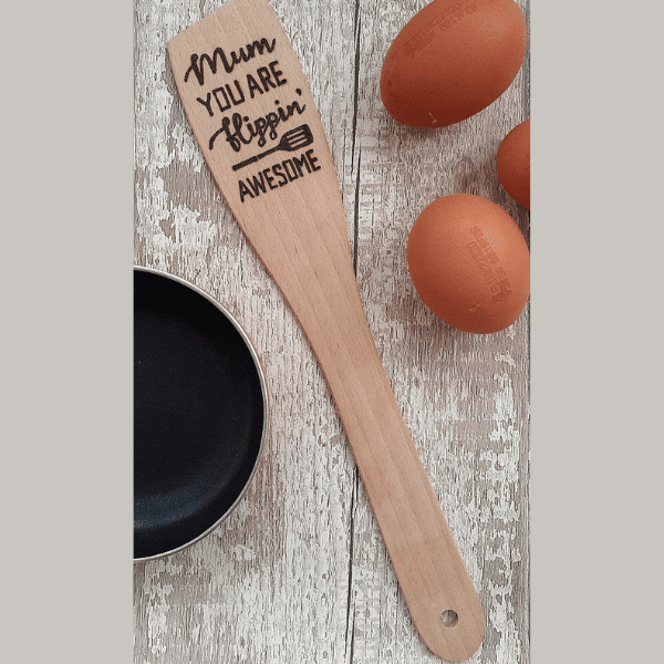 "Wooden spatula with hand-burnt text: 'Mum, you're flippin' awesome.'"