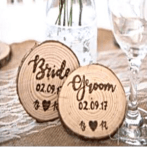 A photograph showcasing rustic personalized place settings and wedding favors. The place settings consist of wooden table cards with engraved names, accompanied by small glass jars filled with wildflowers.