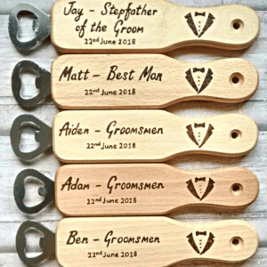A close-up image of a personalized wooden bottle opener. The opener is made from high-quality wood and has a smooth, polished surface. It features a custom engraving of the recipient's name and a decorative design, adding a personal touch. The opener has a sturdy metal mechanism at one end with a curved shape, ideal for effortlessly popping open bottle caps.