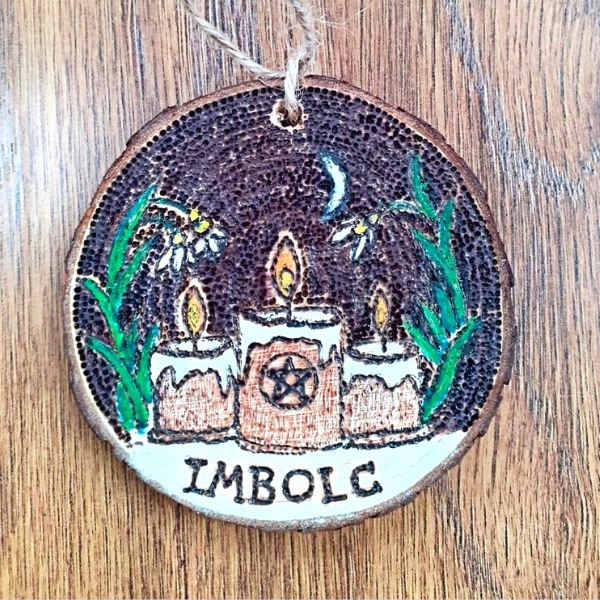 A wooden hanging sign for Imbolc featuring a candle design. The sign is crafted from natural wood and depicts a vibrant candle at its center, surrounded by delicate floral patterns. The candle's flame shines brightly, symbolizing the warmth and renewal associated with the traditional Celtic festival of Imbolc."