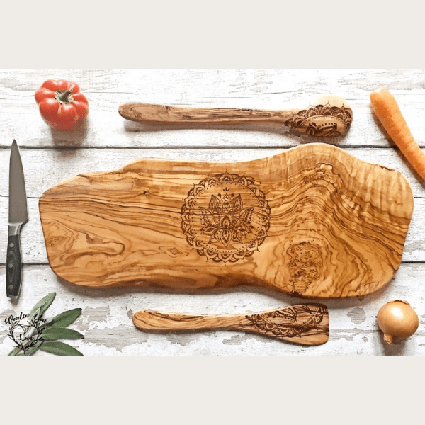 An image description of an olive wood board, accompanied by a spoon and spatula, all adorned with a meticulously hand-burnt mandala design. The olive wood board is rectangular in shape, displaying a rich grain pattern with natural variations in color. On the board's surface, a symmetrical and intricate mandala design has been meticulously etched using a wood-burning technique. The design features geometric patterns, floral motifs, and delicate linework, all carefully arranged to create a captivating visual. Adjacent to the board, a wooden spoon and spatula complement the design with matching burnt mandala motifs on their handles. The craftsmanship and attention to detail in this handcrafted set elevate its aesthetic appeal and make it a unique addition to any kitchen or culinary display."